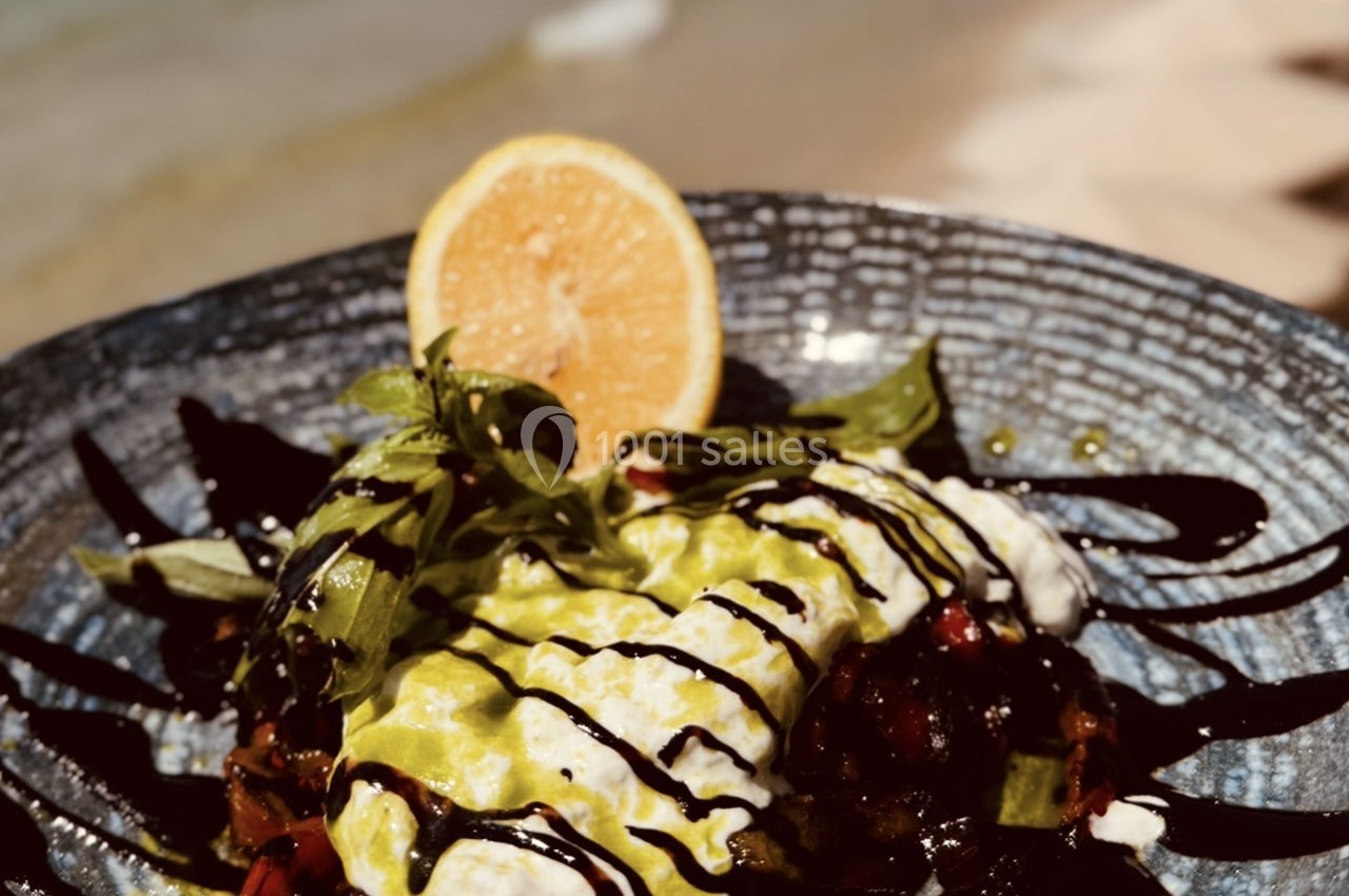 Assiette garnie de légumes, sauce crémeuse, filet de vinaigre balsamique et tranche de citron, en bord de mer.