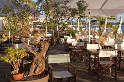Plateau en bois avec verrines garnies de crevettes, tomates, olives et herbes fraîches, disposées sur une nappe beige.