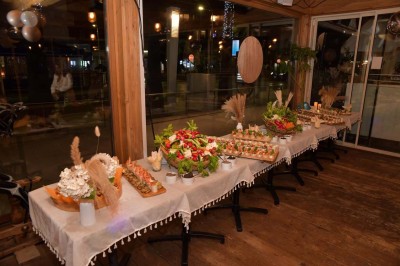 Plateau en bois avec verrines garnies de crevettes, tomates, olives et herbes fraîches, disposées sur une nappe beige.