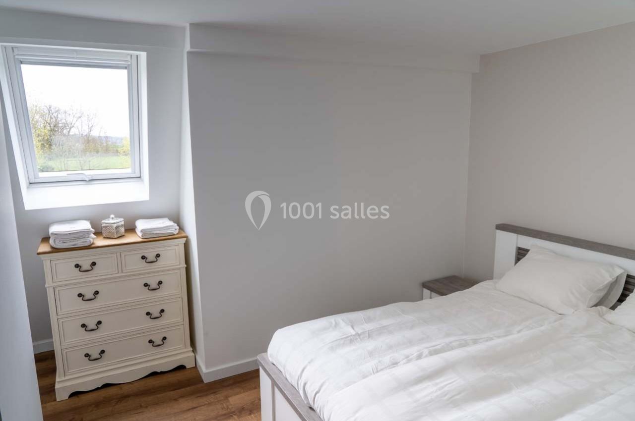 Chambre lumineuse avec un lit simple, une commode blanche, un mur clair et une fenêtre donnant sur l'extérieur.