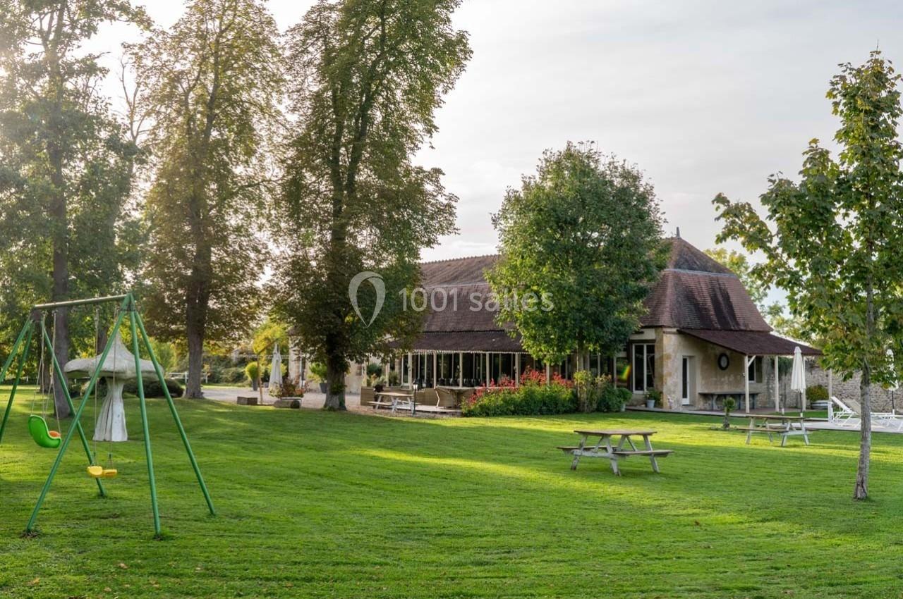Bâtiment en pierre entouré d'arbres, avec une aire de jeux, des tables de pique-nique et une pelouse bien entretenue.