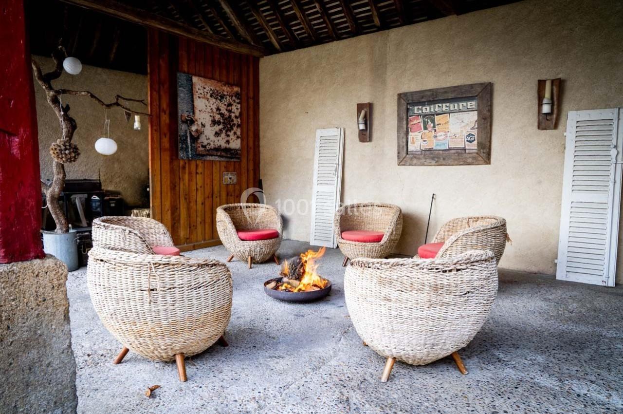 Espace extérieur couvert avec fauteuils en rotin autour d'un brasero allumé, décor mural et ambiance chaleureuse.