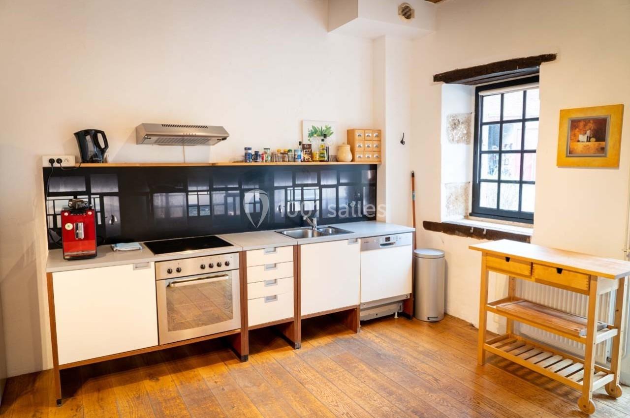 Cuisine lumineuse avec plancher en bois, meubles blancs, électroménagers modernes et fenêtre laissant entrer la lumière…