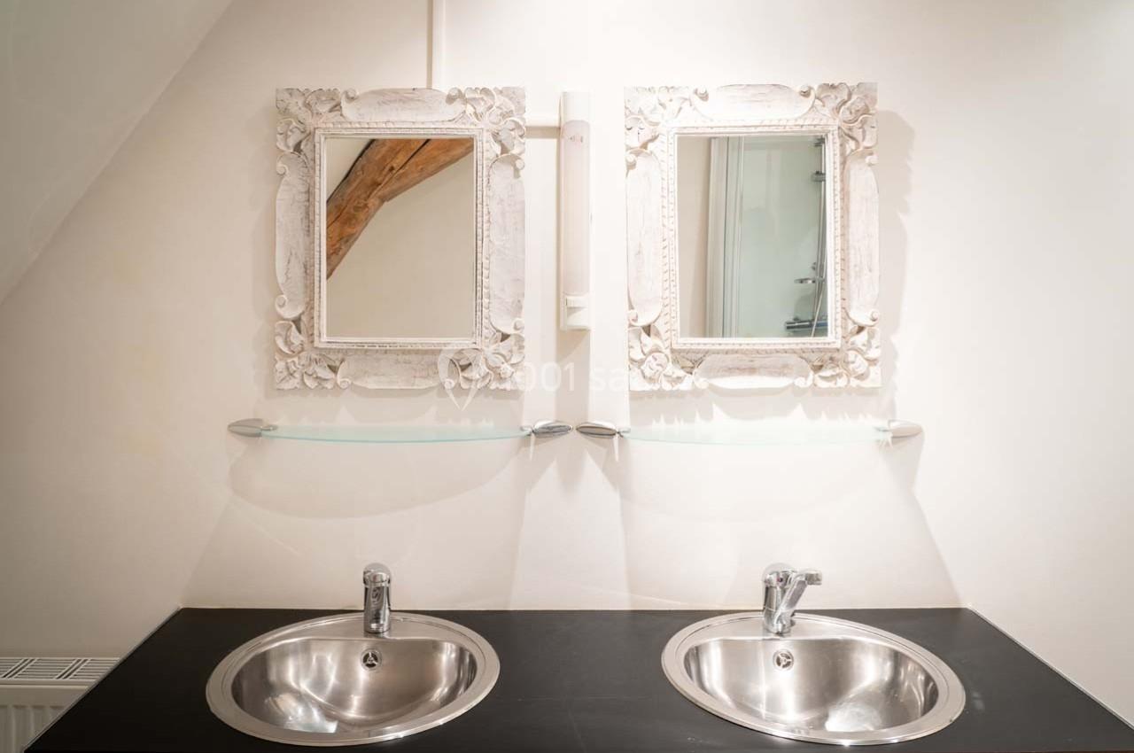 Deux lavabos en acier inoxydable avec miroirs encadrés de blanc, sur un plan de travail sombre dans une salle de bain…