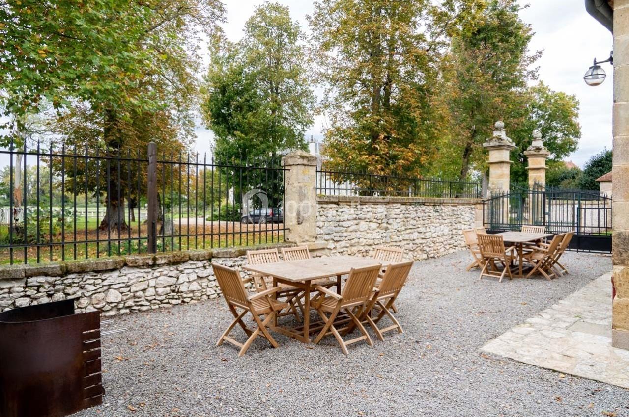 Terrasse extérieure avec tables et chaises en bois, entourée d'arbres et d'une clôture en fer forgé.