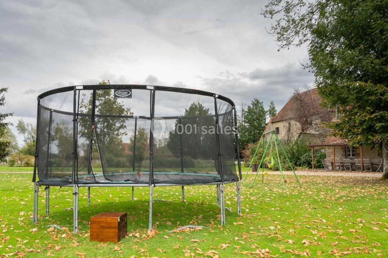 Trampoline rond avec filet de sécurité installé dans un jardin verdoyant, près d'une maison en pierre.