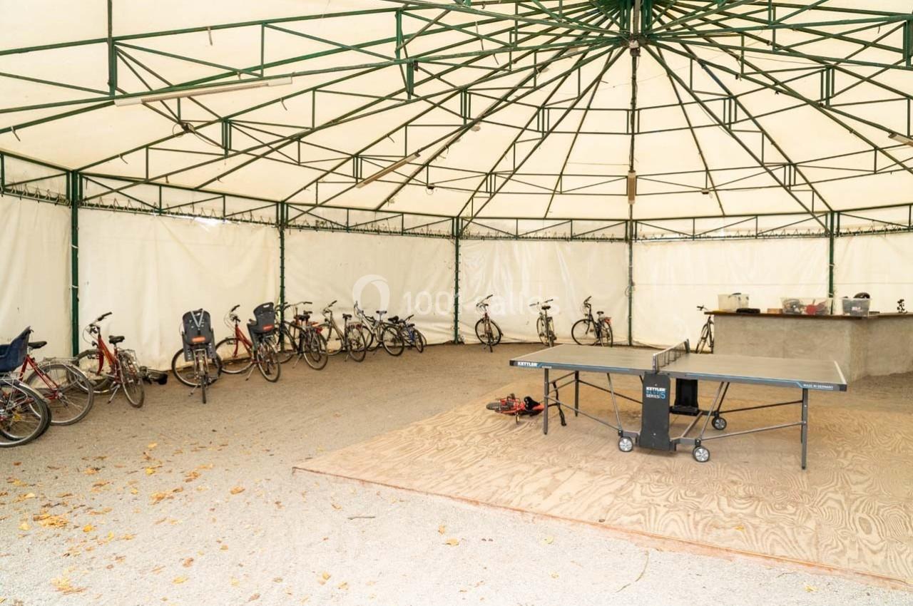 Abri avec vélos alignés, table de ping-pong et comptoir sur un sol en bois et gravier.