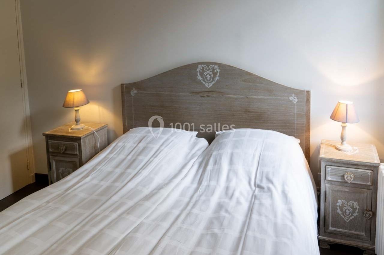 Lit double avec draps blancs, encadré par deux tables de chevet en bois clair avec lampes allumées.