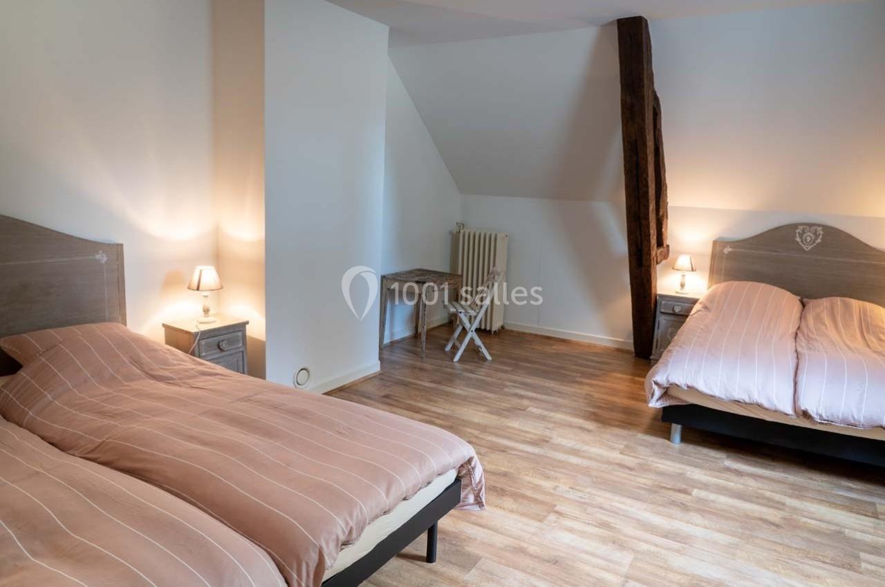 Chambre avec deux lits simples, parquet au sol, bureau en bois clair et poutre apparente.