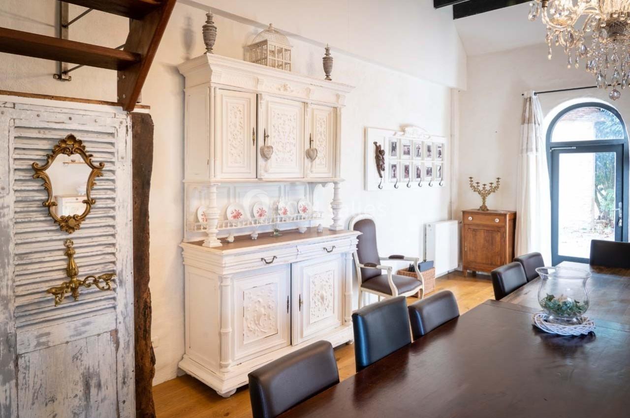 Salle à manger lumineuse avec une grande table en bois, un buffet blanc ancien et des éléments décoratifs élégants.