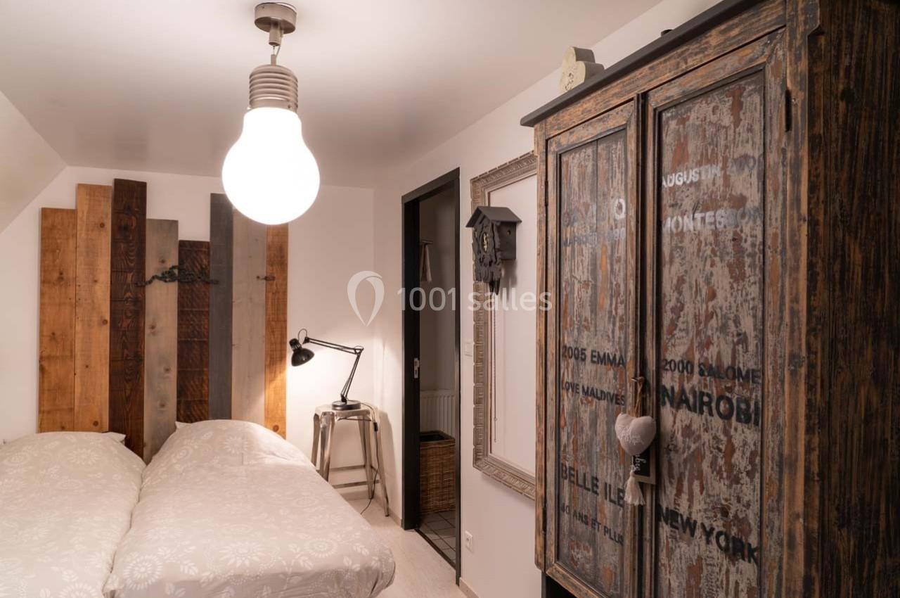 Chambre avec lit double, armoire en bois rustique, lampe suspendue et décoration murale en bois.
