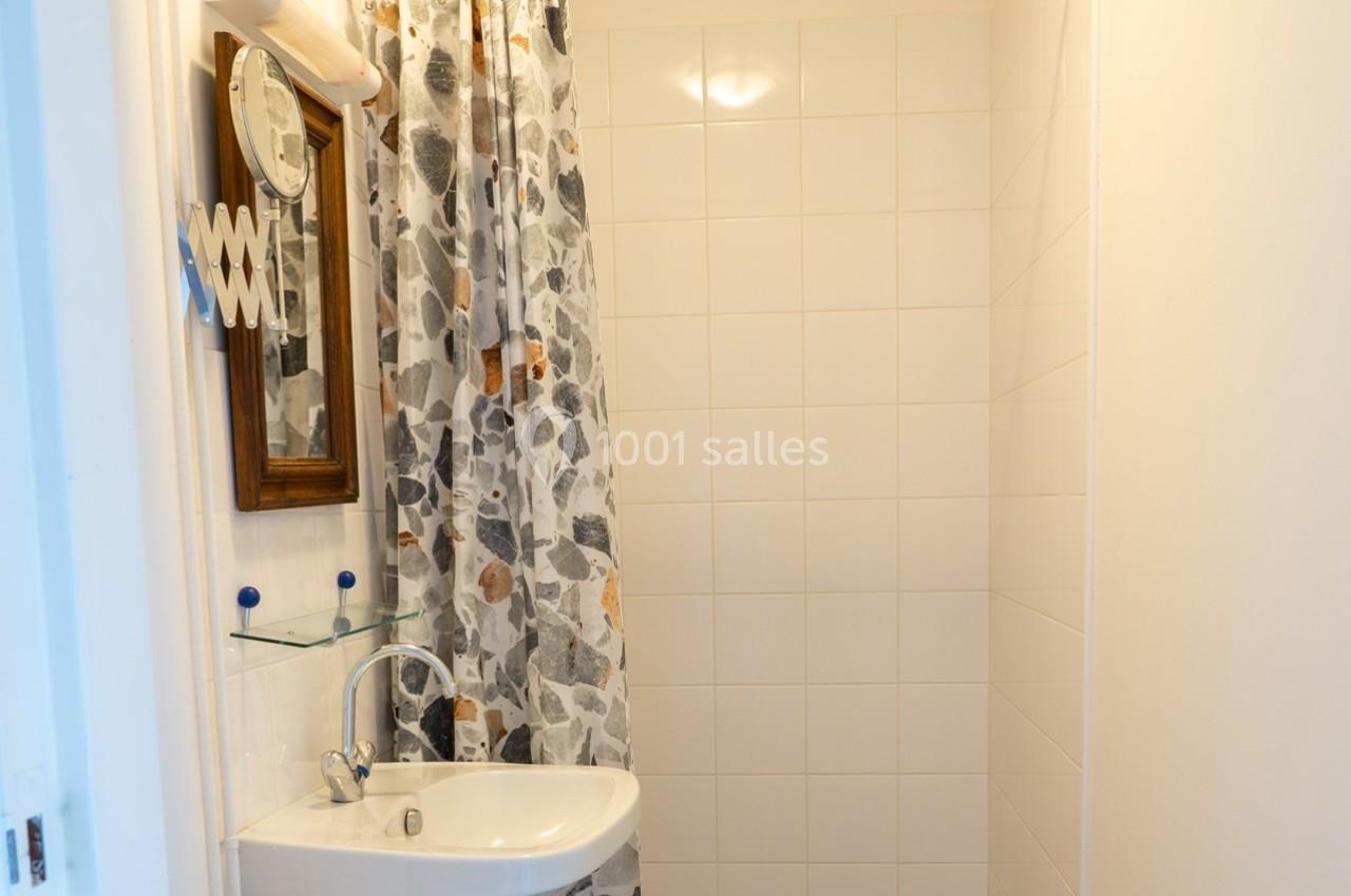Lavabo blanc avec miroir en bois, rideau de douche à motifs et carrelage mural blanc dans une petite salle de bain.