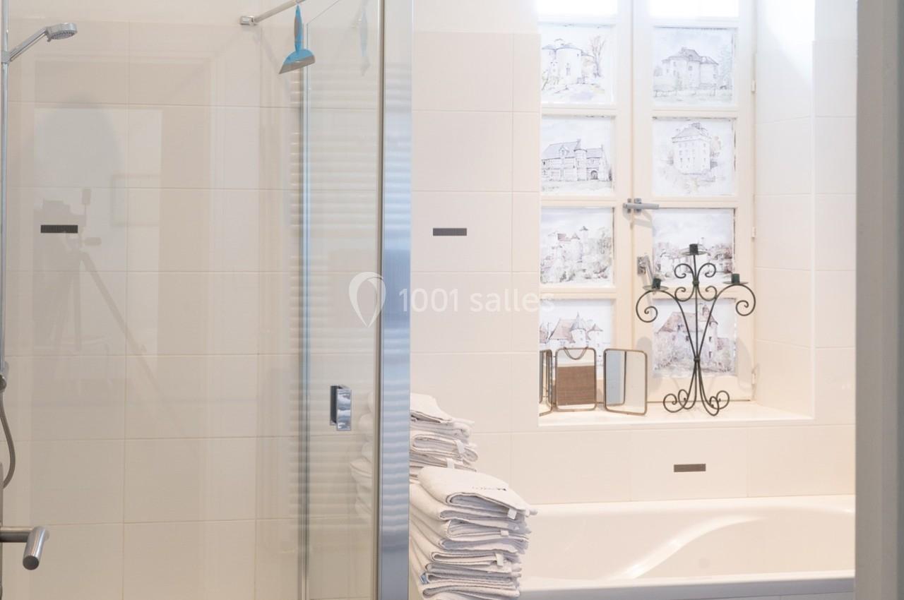Salle de bain lumineuse avec douche vitrée, baignoire, pile de serviettes blanches et fenêtre décorée.