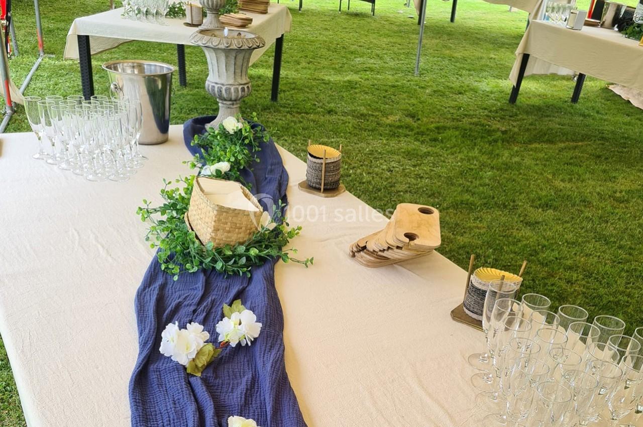 Table décorée pour un événement en extérieur avec nappes, fleurs, verres à pied et accessoires en bois.