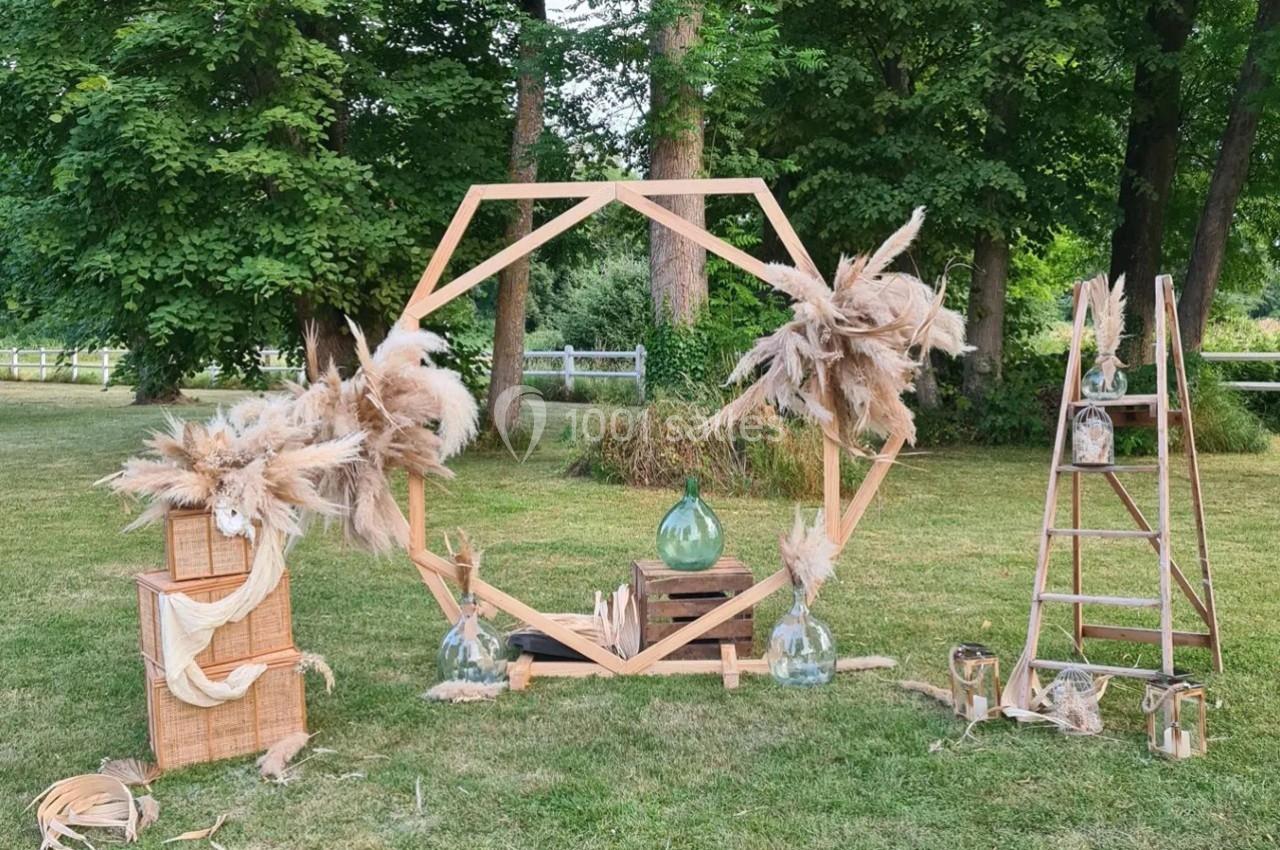Décoration champêtre avec structure en bois, pampas, échelle et paniers sur une pelouse entourée d'arbres.