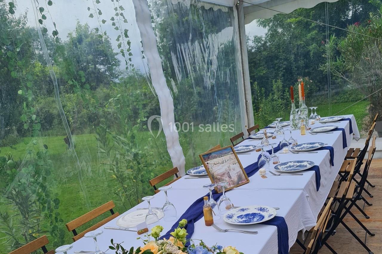 Table dressée sous une tente transparente, avec nappes blanches, vaisselle élégante et décoration florale.