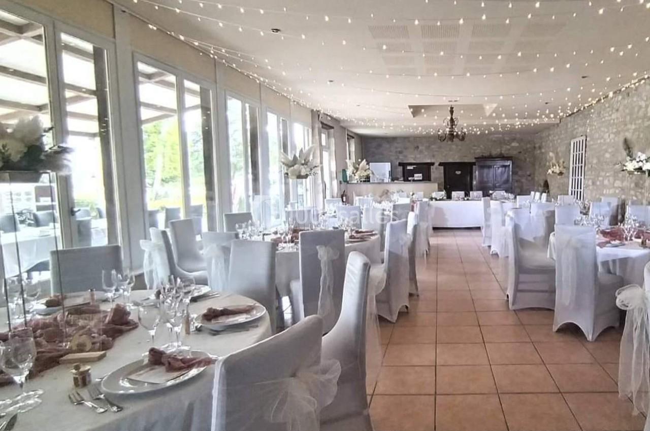 Salle de réception décorée avec des tables dressées, nappes blanches et guirlandes lumineuses suspendues au plafond.