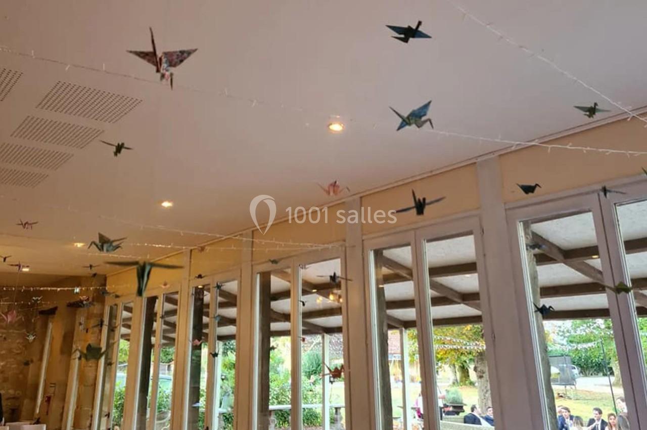 Guirlandes de grues en papier suspendues au plafond d'une salle lumineuse avec vue sur un jardin extérieur.