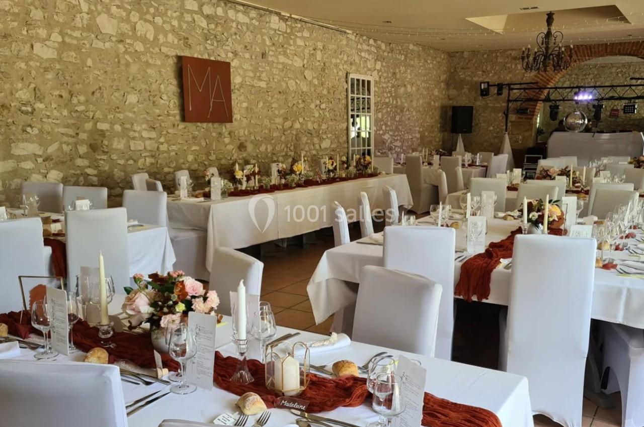 Salle de réception décorée avec des tables dressées, nappes blanches, chemins de table rouges et arrangements floraux.