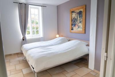 Chambre lumineuse avec deux lits simples, un miroir mural, un fauteuil en osier et un tableau décoratif.