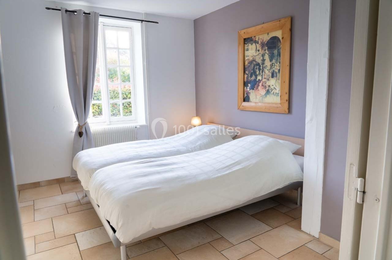 Chambre lumineuse avec deux lits simples, murs clairs, tableau encadré et fenêtre donnant sur un jardin.