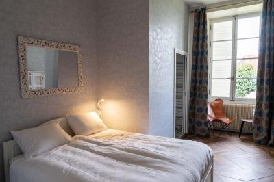 Chambre lumineuse avec deux lits simples, un miroir mural, un fauteuil en osier et un tableau décoratif.