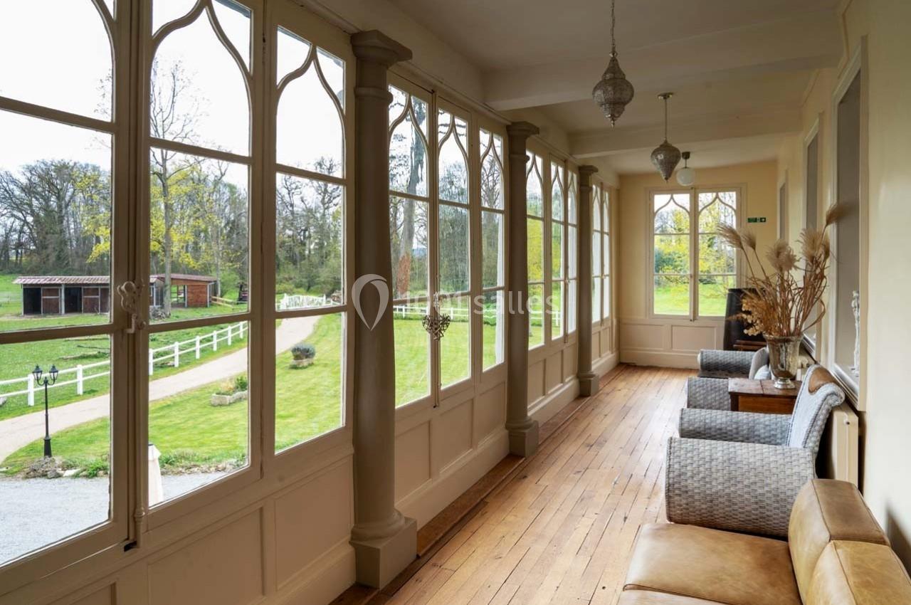 Véranda lumineuse avec parquet en bois, fauteuils et vue sur un jardin verdoyant et une allée gravillonnée.