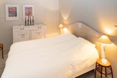 Chambre lumineuse avec deux lits simples, un miroir mural, un fauteuil en osier et un tableau décoratif.