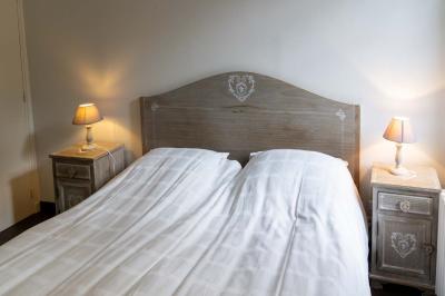 Chambre lumineuse avec deux lits simples, un miroir mural, un fauteuil en osier et un tableau décoratif.