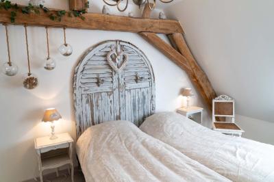 Chambre lumineuse avec deux lits simples, un miroir mural, un fauteuil en osier et un tableau décoratif.