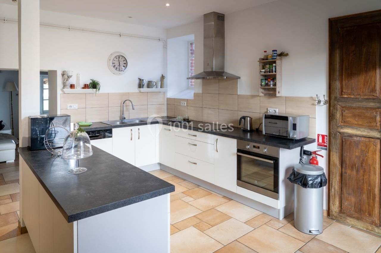 Cuisine moderne avec plan de travail noir, meubles blancs, électroménagers en inox et sol en carrelage beige.