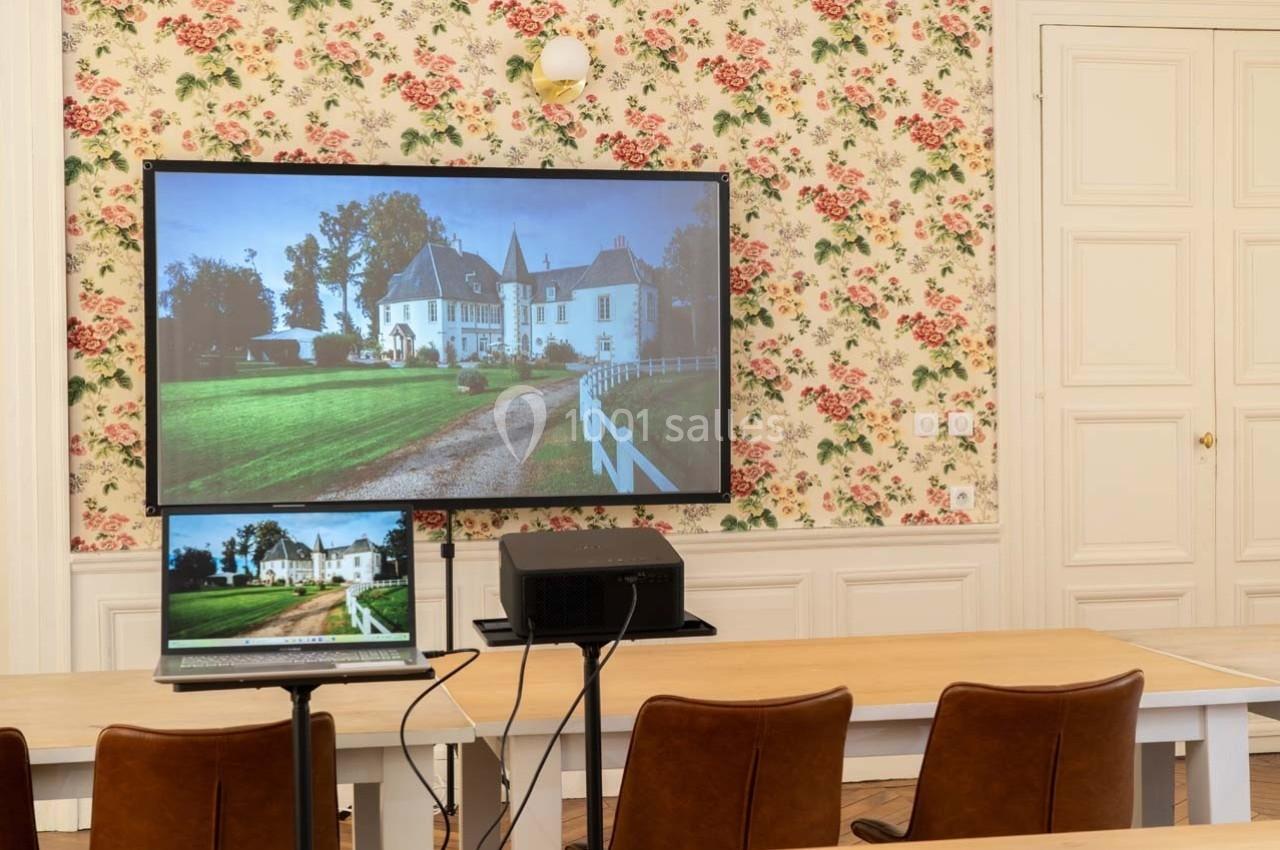 Écran projetant l'image d'un château, installé dans une salle avec des tables, des chaises et un mur à motif floral.