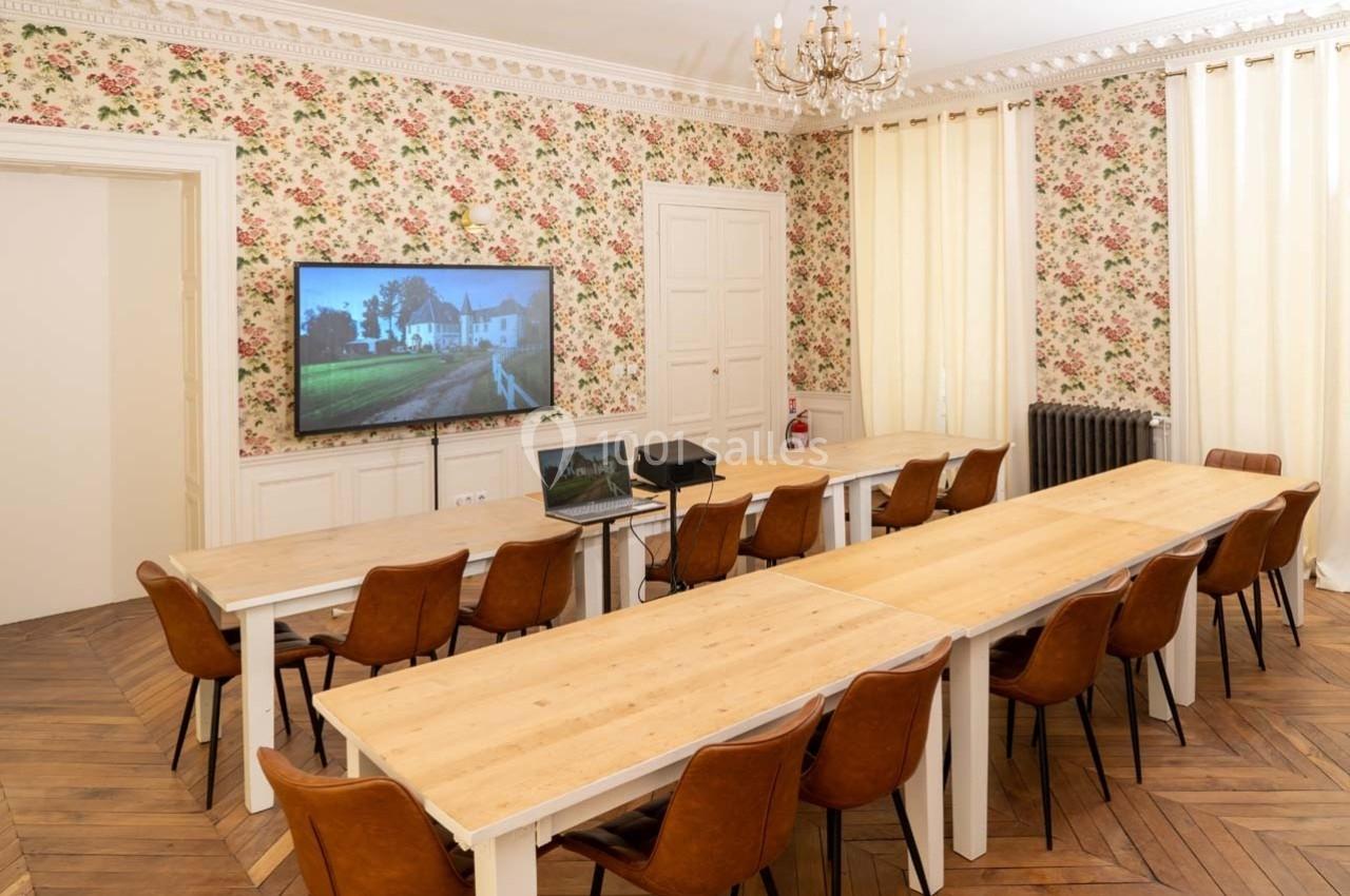 Salle de réunion lumineuse avec tables en bois, chaises en cuir, écran mural et murs ornés de papier peint fleuri.
