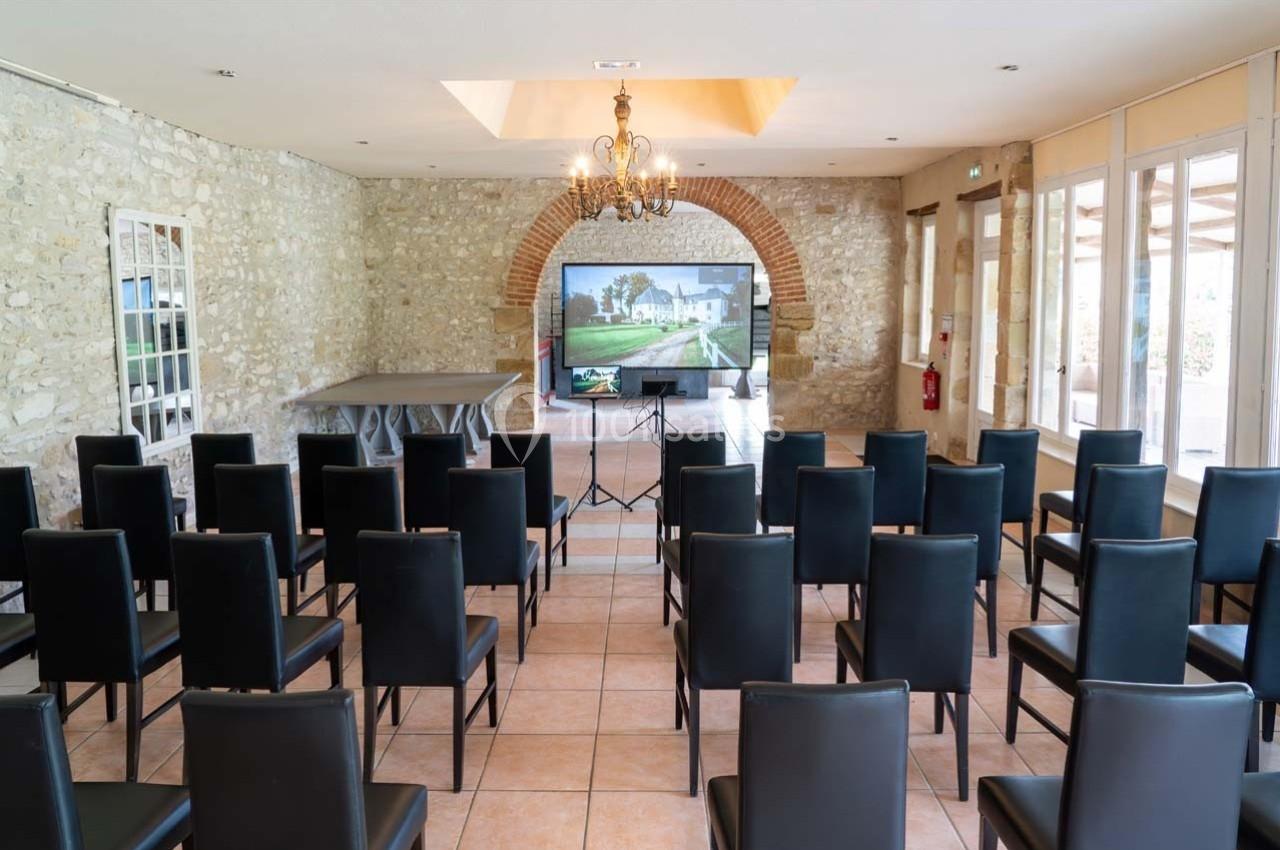 Salle de réunion avec des chaises noires alignées, un écran de projection et des murs en pierre apparente.