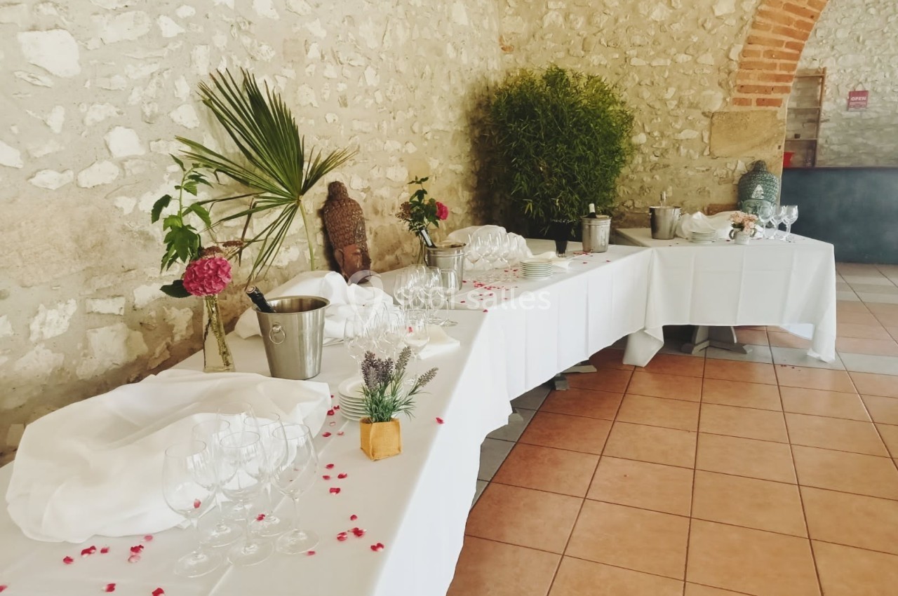 Table dressée avec nappes blanches, verres, seaux à champagne et décorations florales dans une salle en pierre.