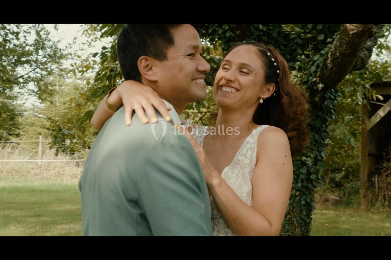Un couple souriant s'enlace devant un arbre dans un jardin ensoleillé.