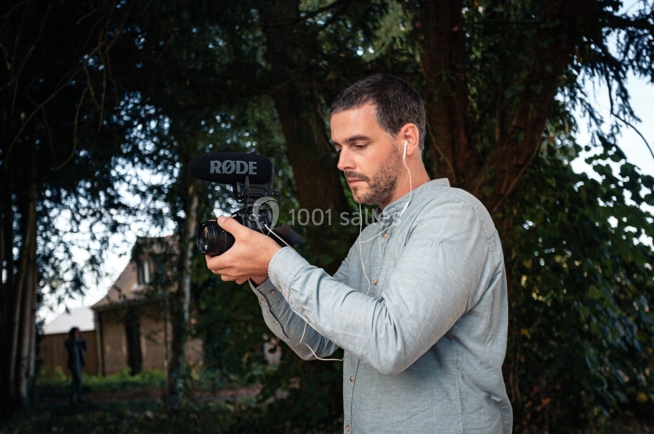 Un homme utilise une caméra équipée d'un microphone externe dans un environnement extérieur boisé.