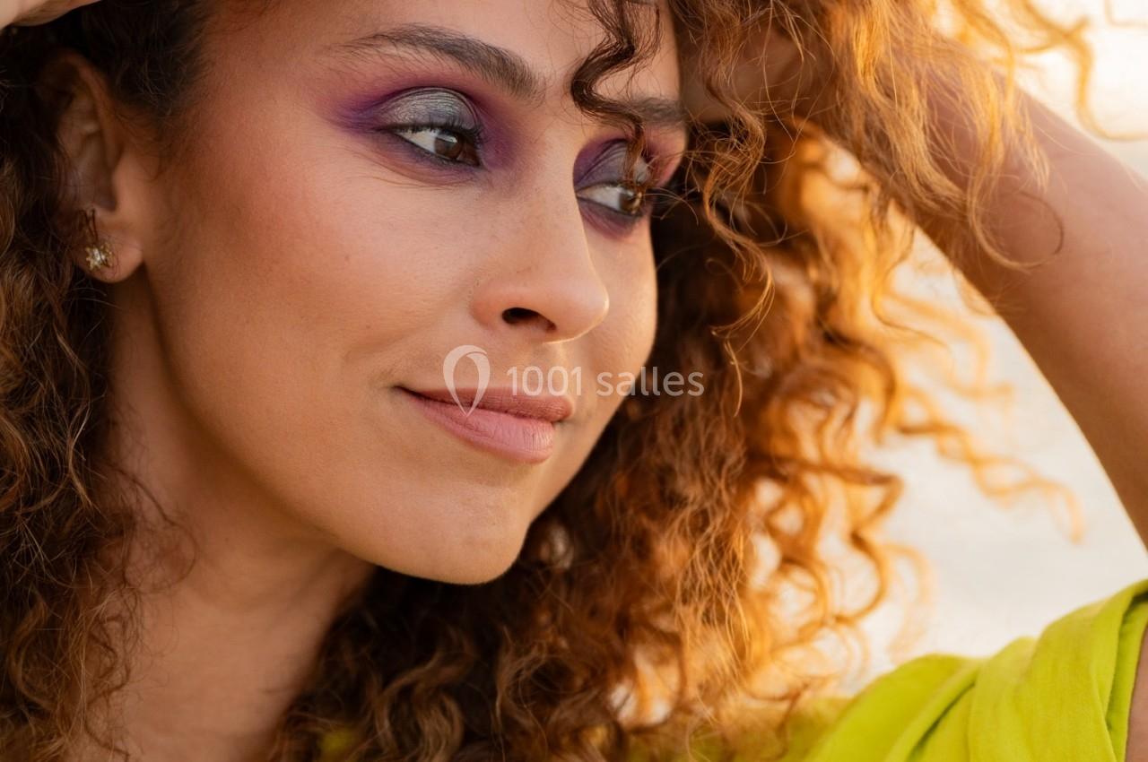 Femme aux cheveux bouclés regardant au loin, vêtue d'une chemise verte, éclairée par une lumière douce.