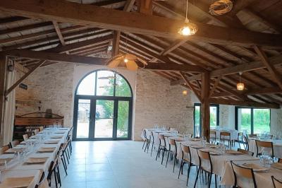 Salle lumineuse avec poutres apparentes, tables dressées et grande baie vitrée donnant sur un extérieur verdoyant.