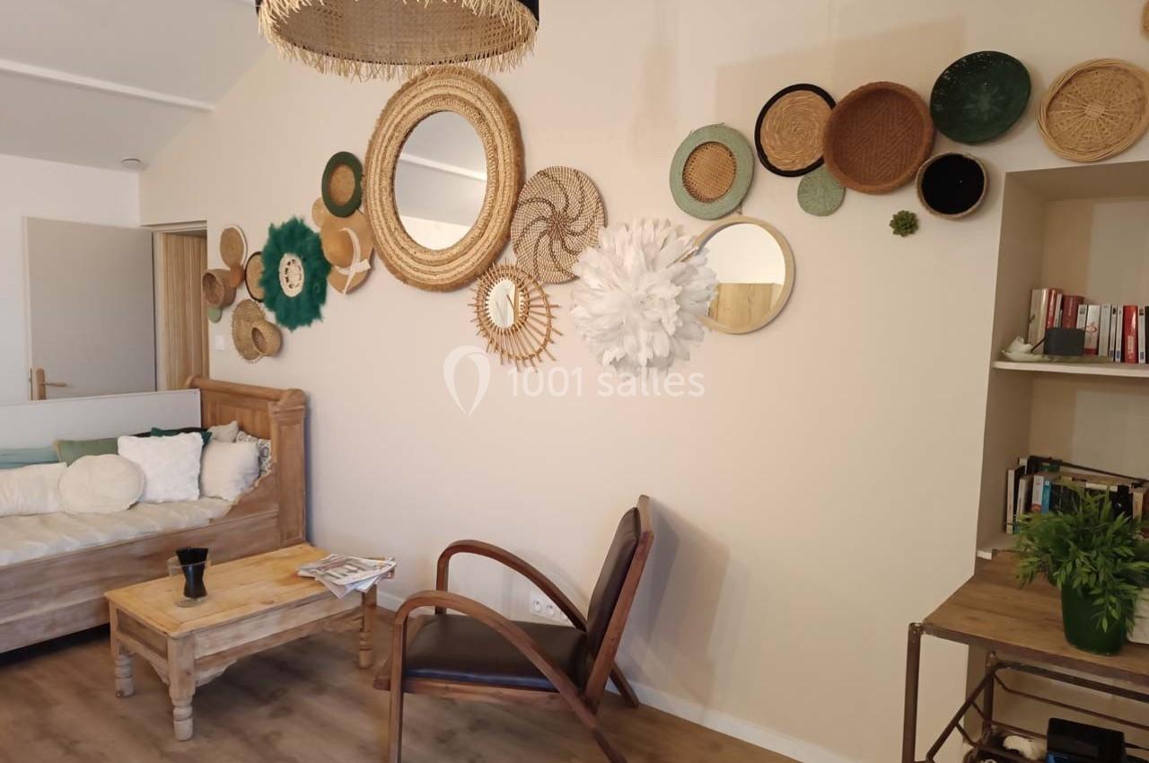 Mur décoré de miroirs et paniers en osier dans un salon avec fauteuil en bois, canapé et étagère.