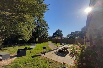 Salle lumineuse avec poutres apparentes, tables dressées et grande baie vitrée donnant sur un extérieur verdoyant.