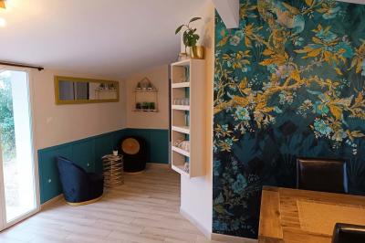 Salle lumineuse avec poutres apparentes, tables dressées et grande baie vitrée donnant sur un extérieur verdoyant.