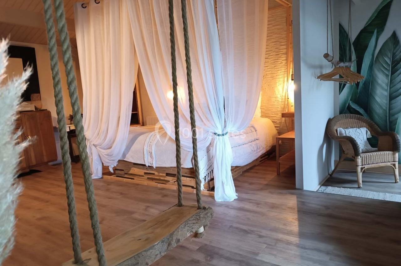 Chambre lumineuse avec lit à baldaquin, balançoire en bois, fauteuil en rotin et décorations végétales.