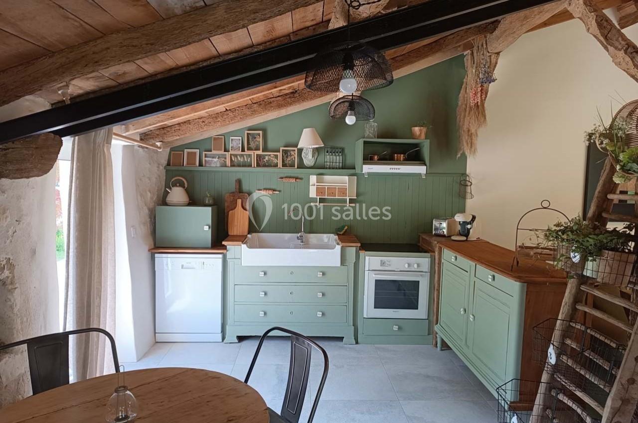 Cuisine rustique avec meubles verts, évier en céramique, poutres apparentes et décoration naturelle en bois et plantes.