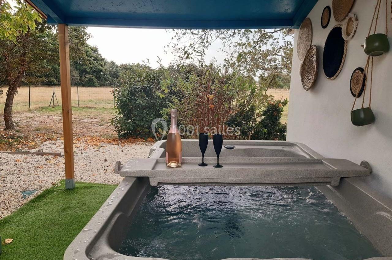 Bain à remous extérieur sous un abri, avec une bouteille de rosé et deux verres posés sur le rebord.