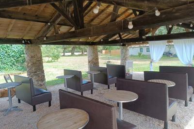 Salle lumineuse avec poutres apparentes, tables dressées et grande baie vitrée donnant sur un extérieur verdoyant.