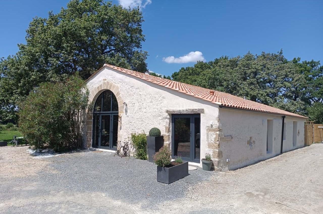 Bâtiment en pierre rénové avec toit en tuiles, grandes ouvertures vitrées et végétation environnante.