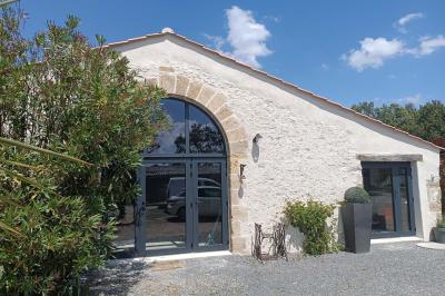 Salle lumineuse avec poutres apparentes, tables dressées et grande baie vitrée donnant sur un extérieur verdoyant.