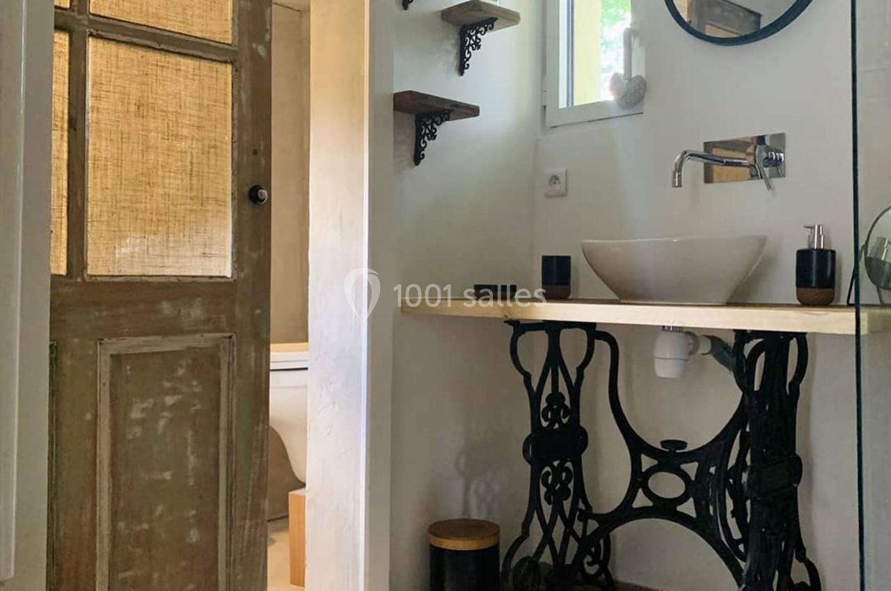 Salle de bain avec lavabo sur pied en métal, miroir rond, étagères murales et porte en bois vieilli.