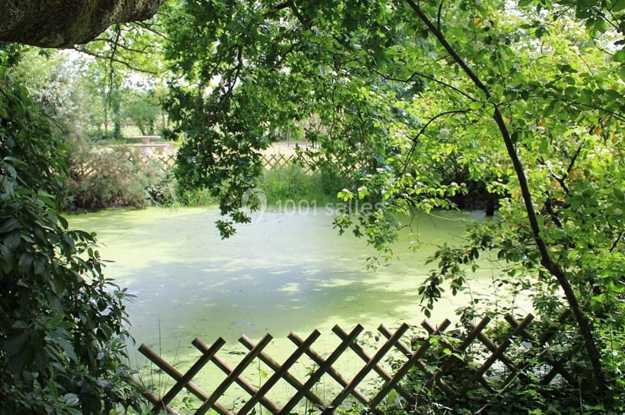 Étang entouré de végétation dense avec une clôture en bois au premier plan.